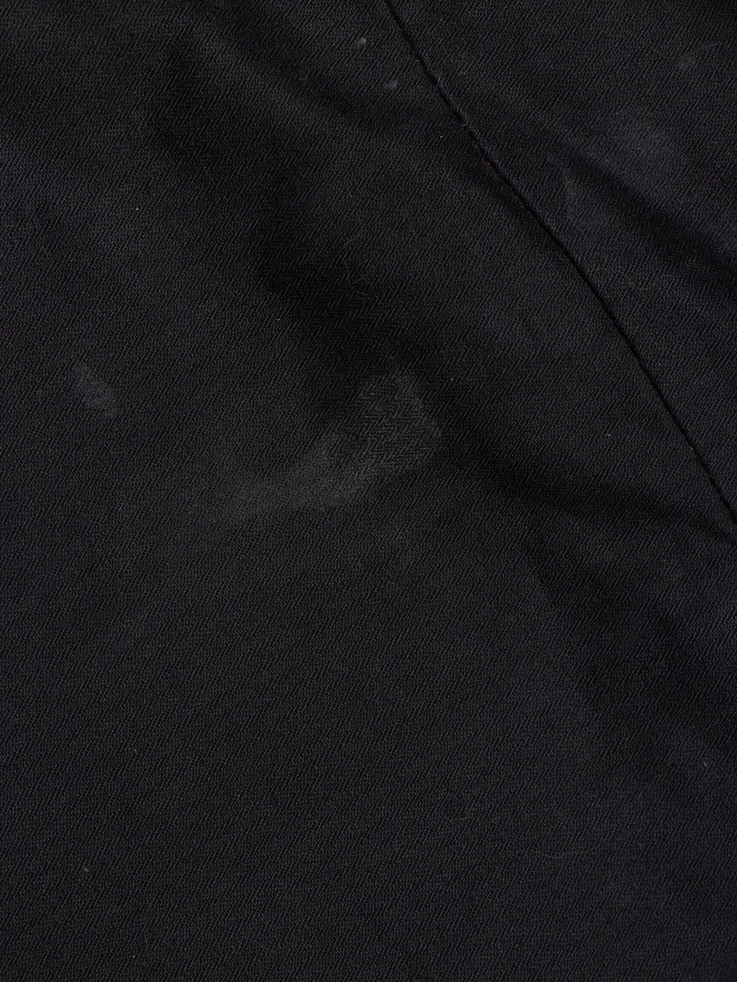 A close-up of black fabric with a visible seam and a slightly mottled texture.