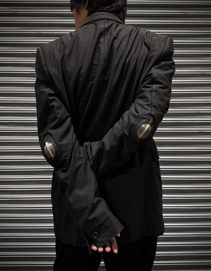 Person wearing a black jacket with metallic elbow pads against a metallic shutter background