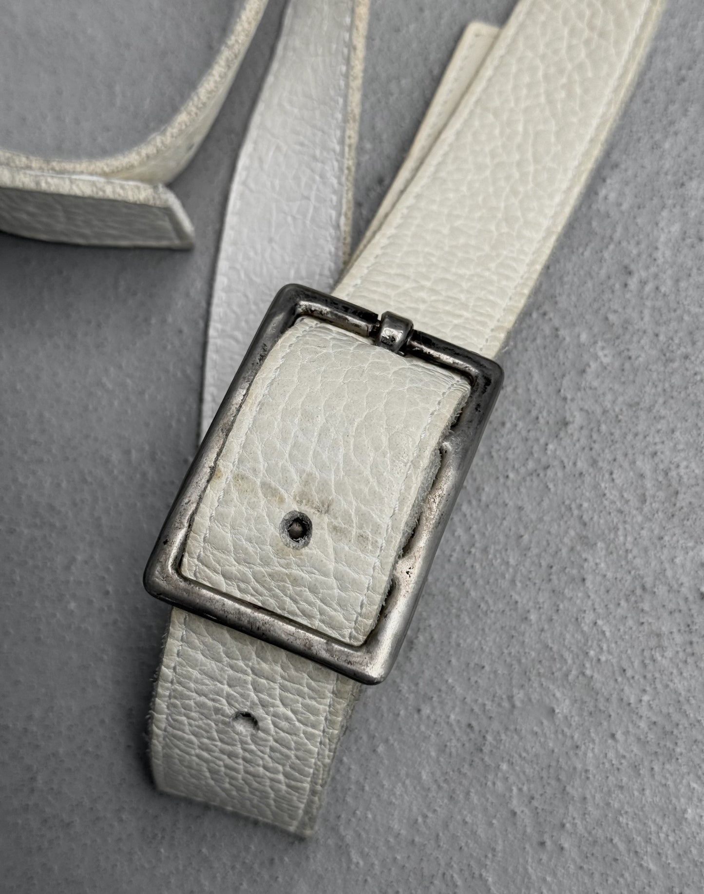 Light gray leather belt with a black buckle on a gray background