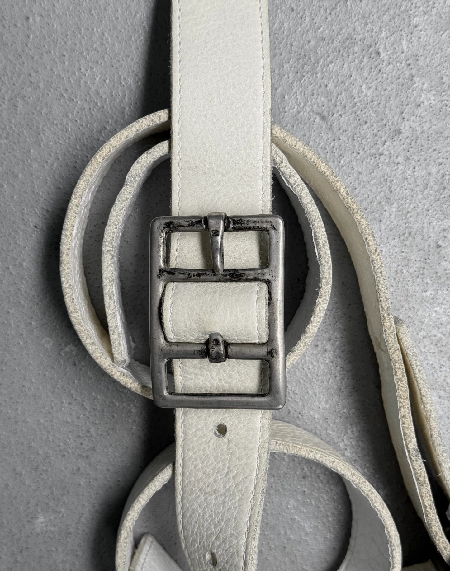 Light gray leather belt with a silver buckle on a gray background