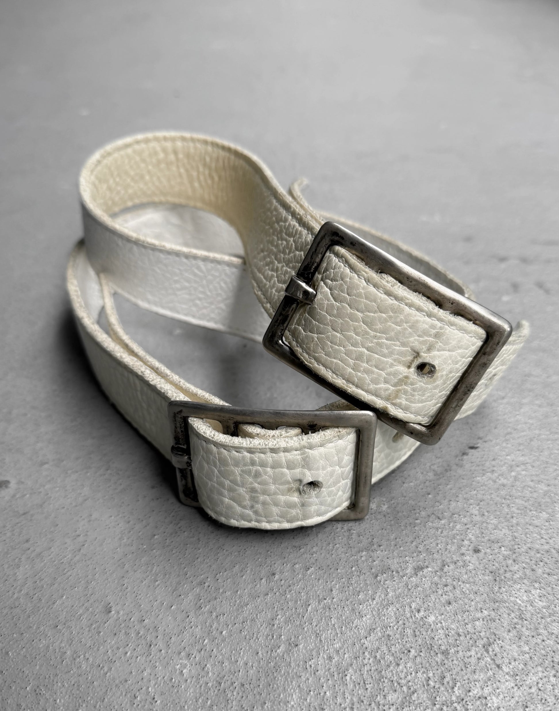 White leather belt with silver buckle on a gray surface