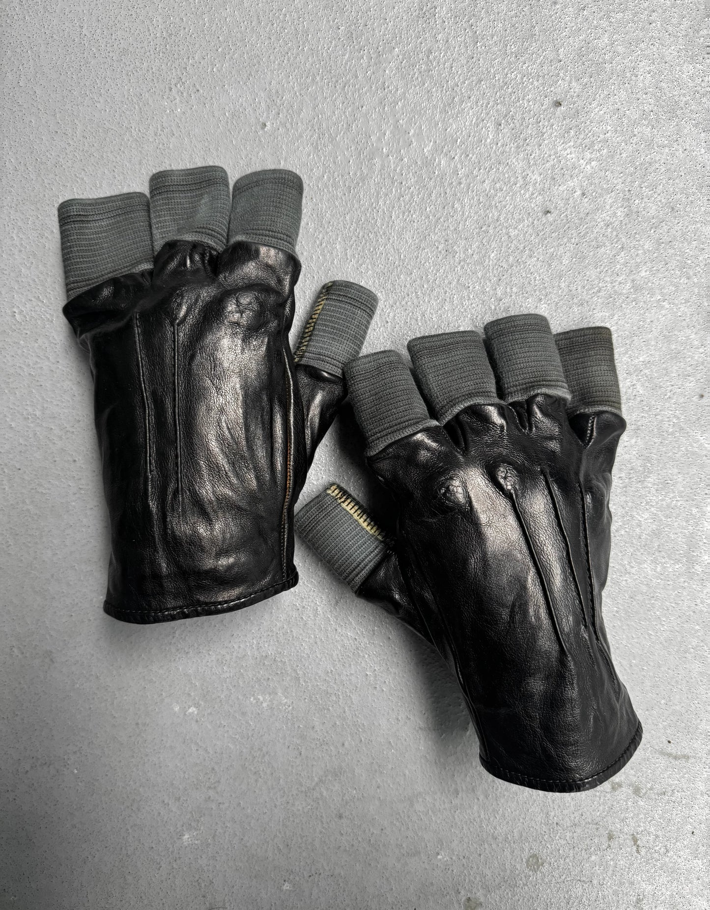 Pair of black leather gloves with gray fingertips on a gray surface