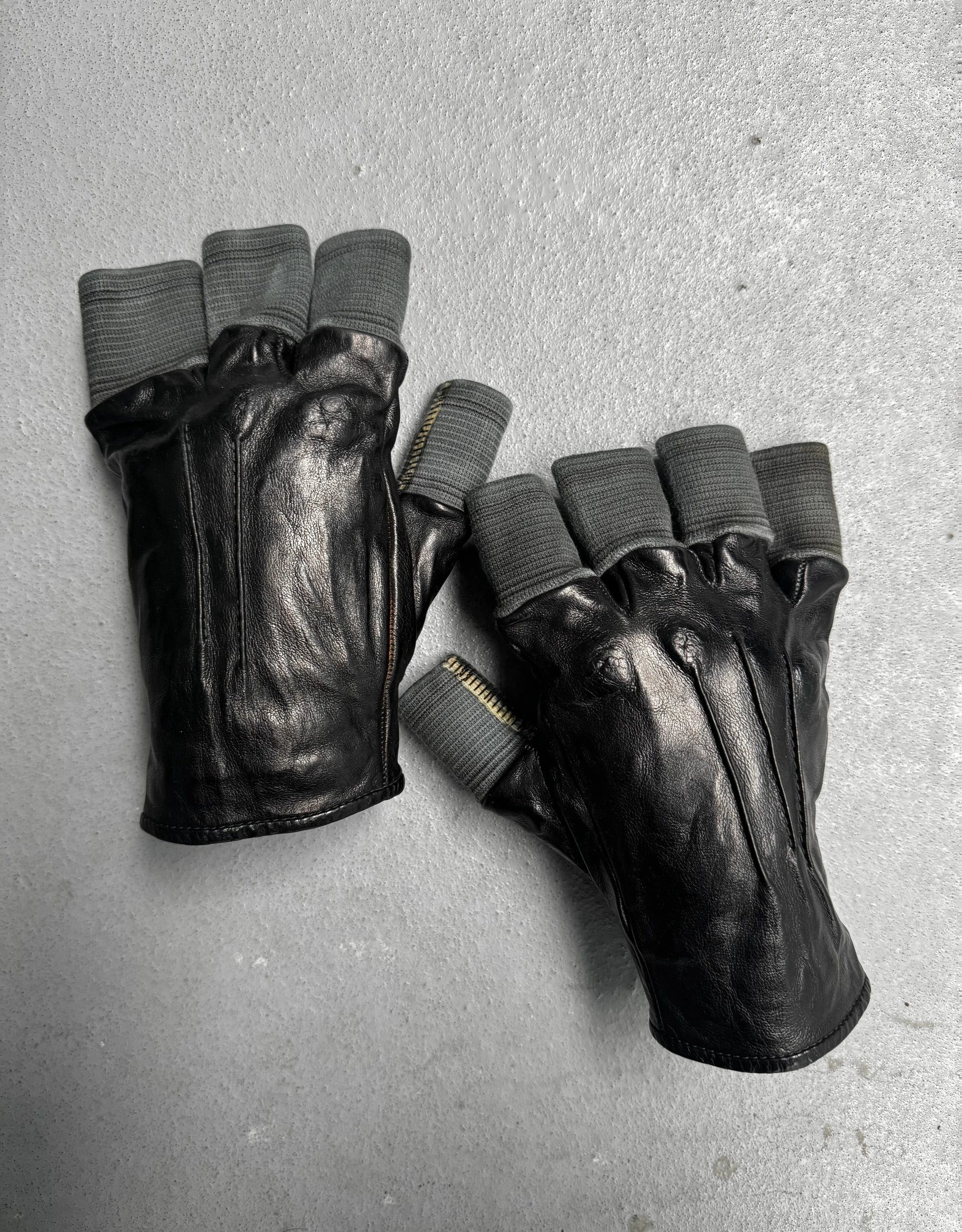 Pair of black leather gloves with gray fingertips on a gray surface