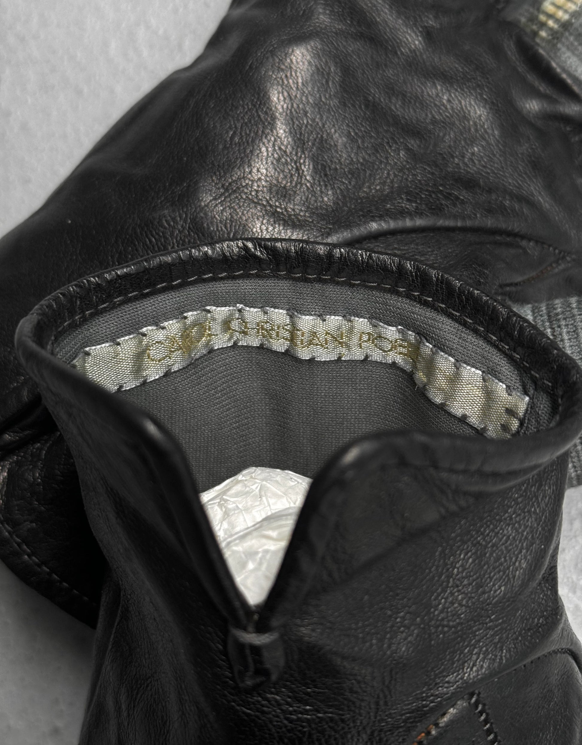 Close-up of black leather glove with brand label on gray background