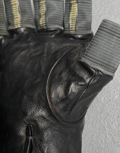 Close-up of a black leather glove with a textured gray strap on a light gray background