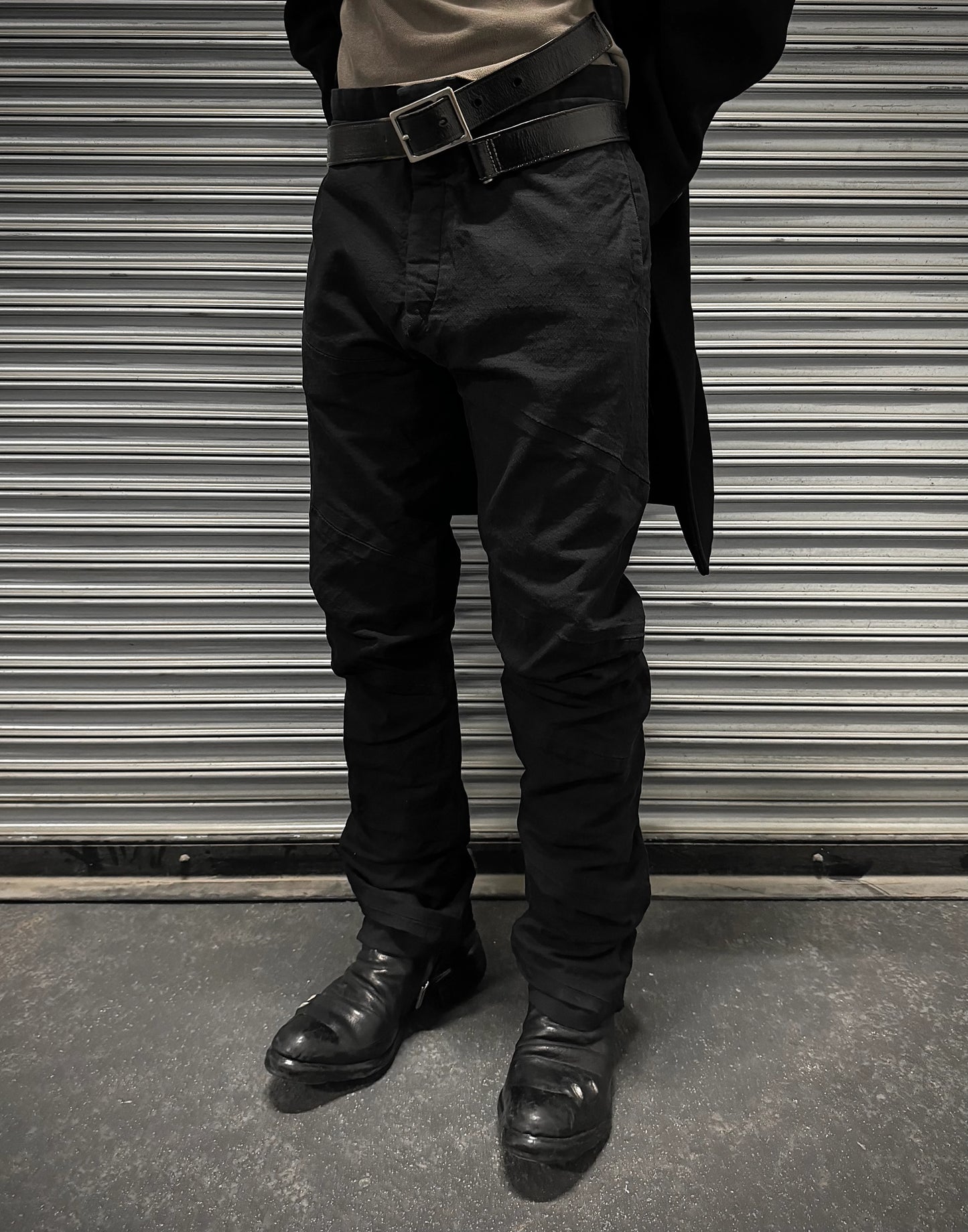 Person wearing black pants and shoes standing in front of a metallic shutter.