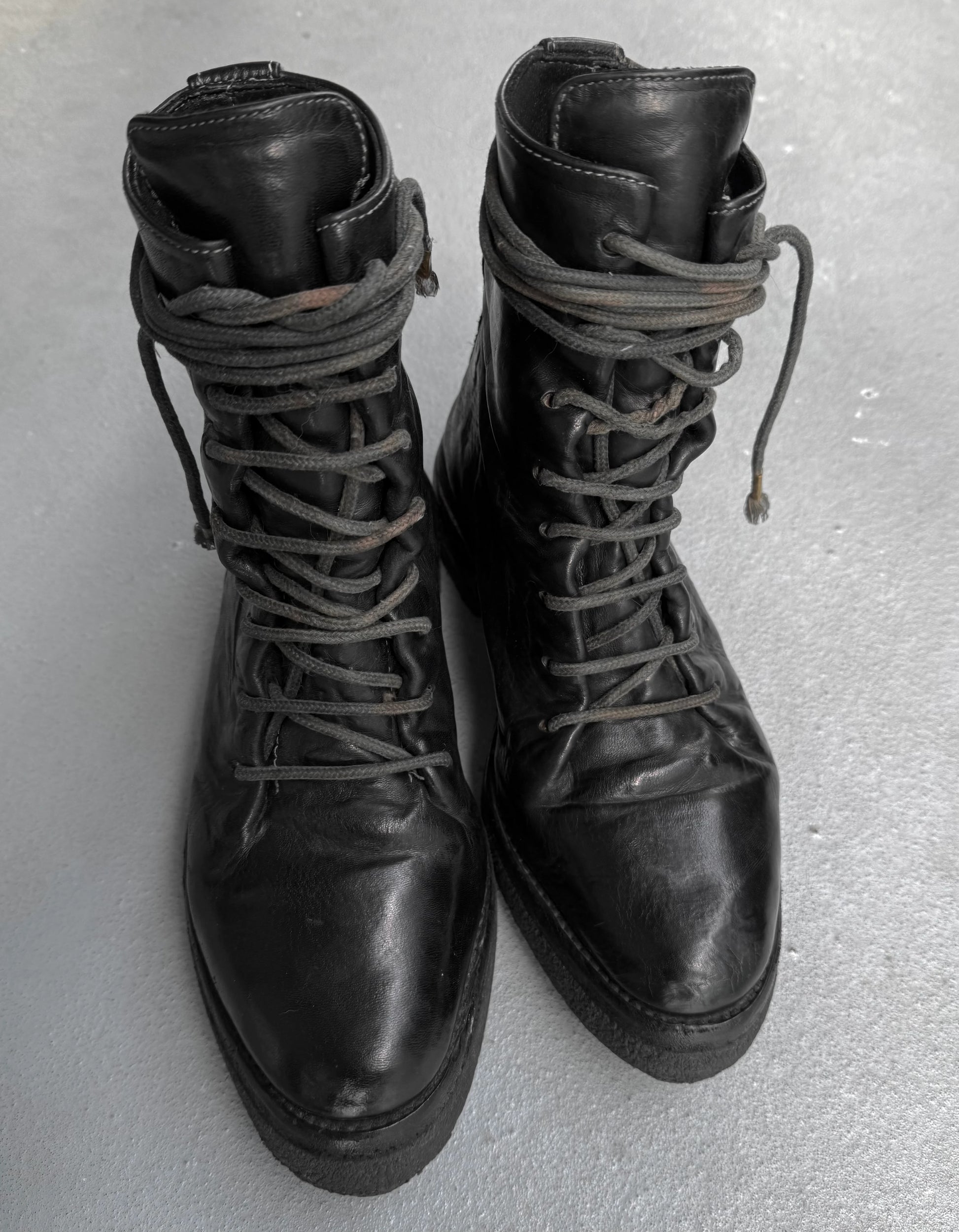 Pair of black leather boots with laces on a light gray background