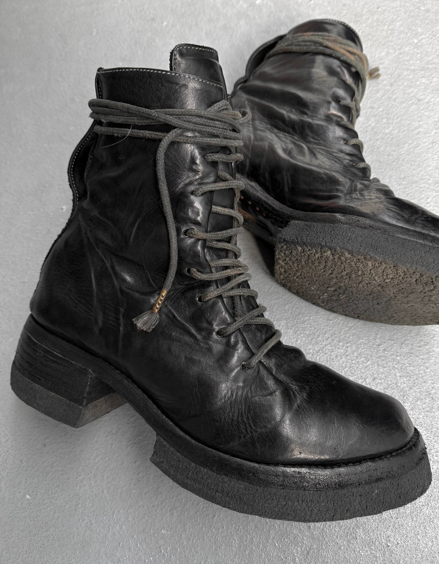 Pair of black leather boots with laces on a light gray background