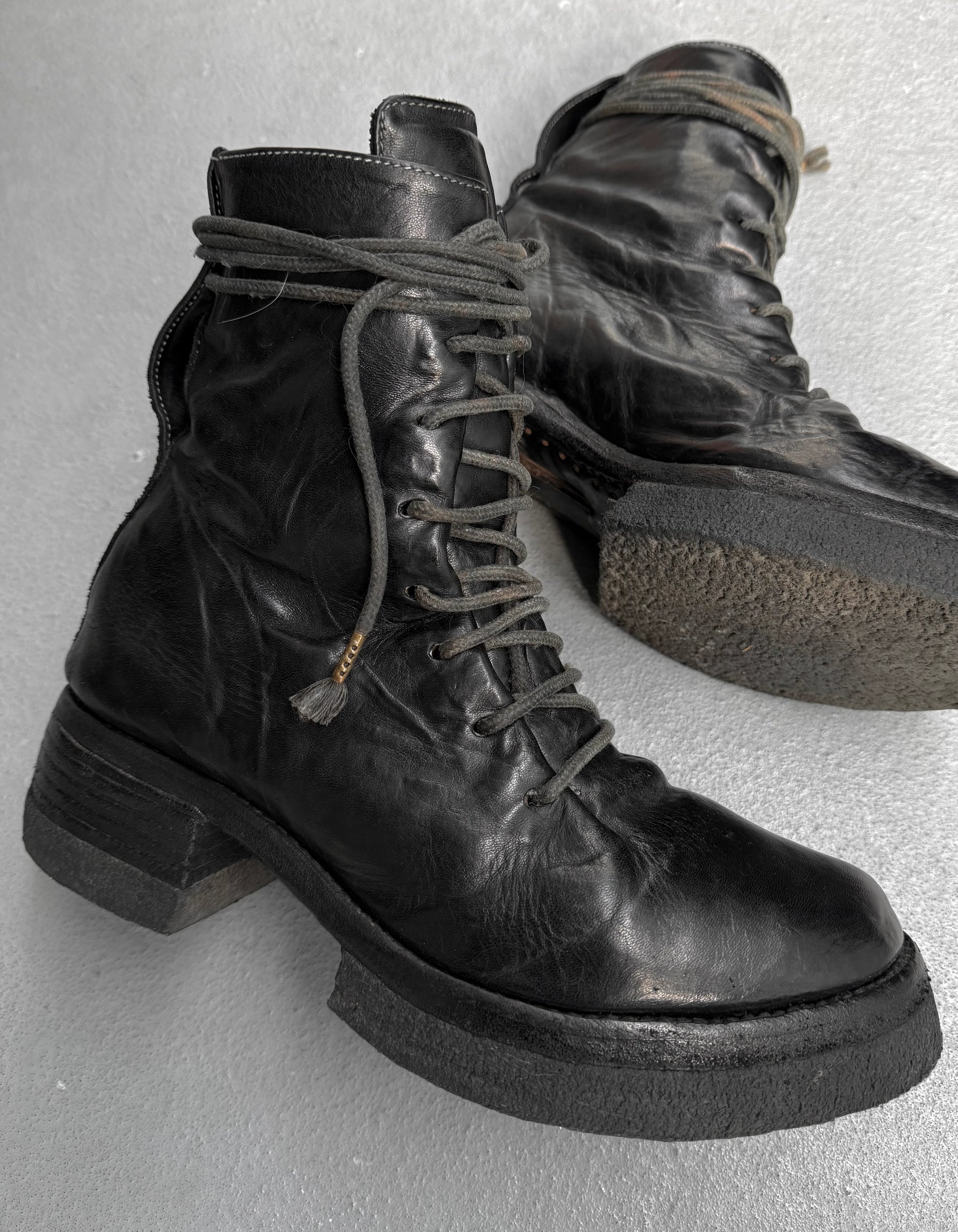 Pair of black leather boots with laces on a light gray background