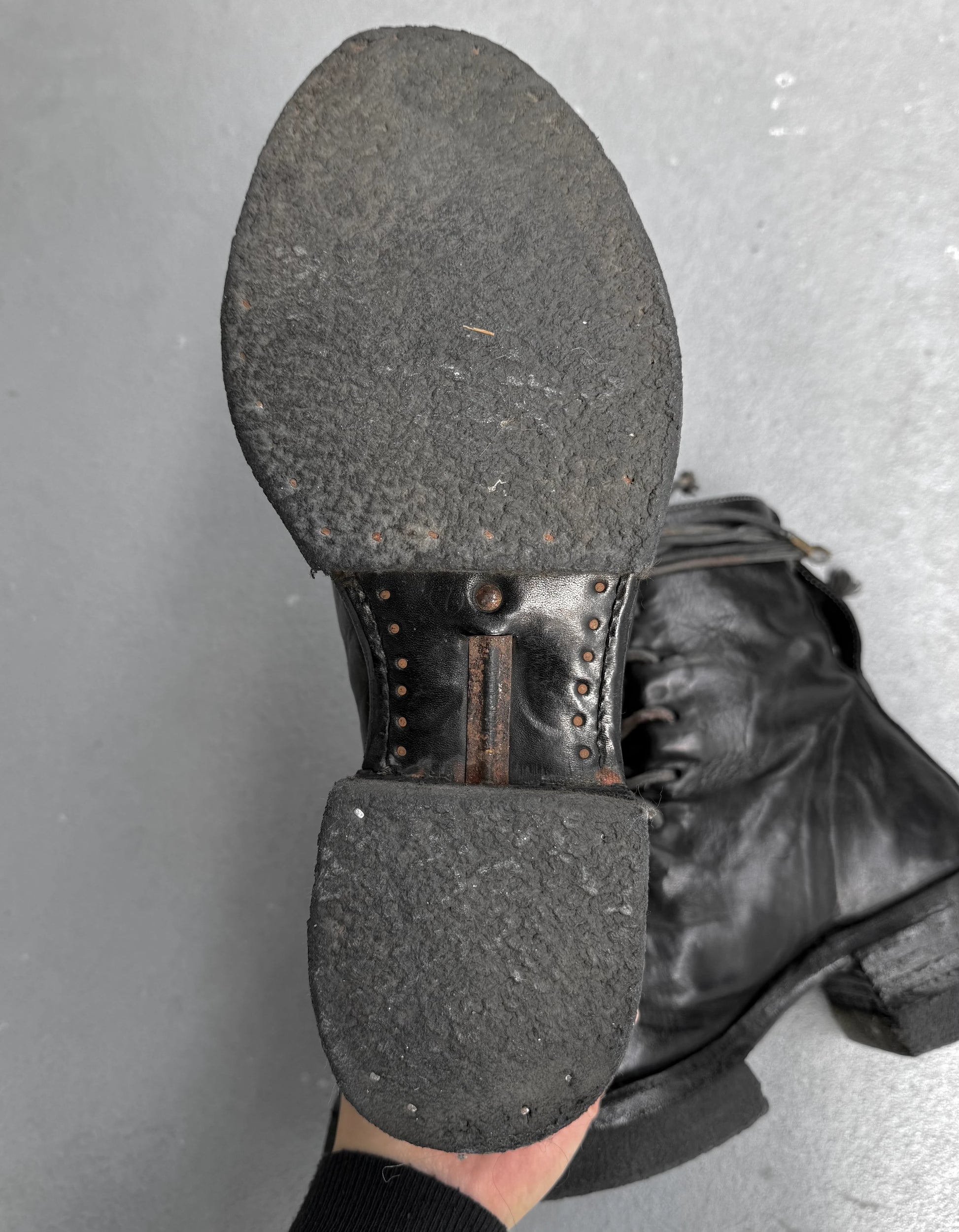 Close-up of a black leather boot sole with metal studs on a gray background