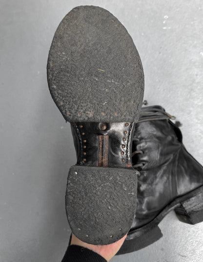 Close-up of a black leather boot sole with metal studs on a gray background
