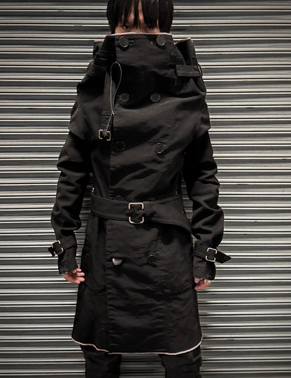 Person wearing a black trench coat with a belt against a metallic background
