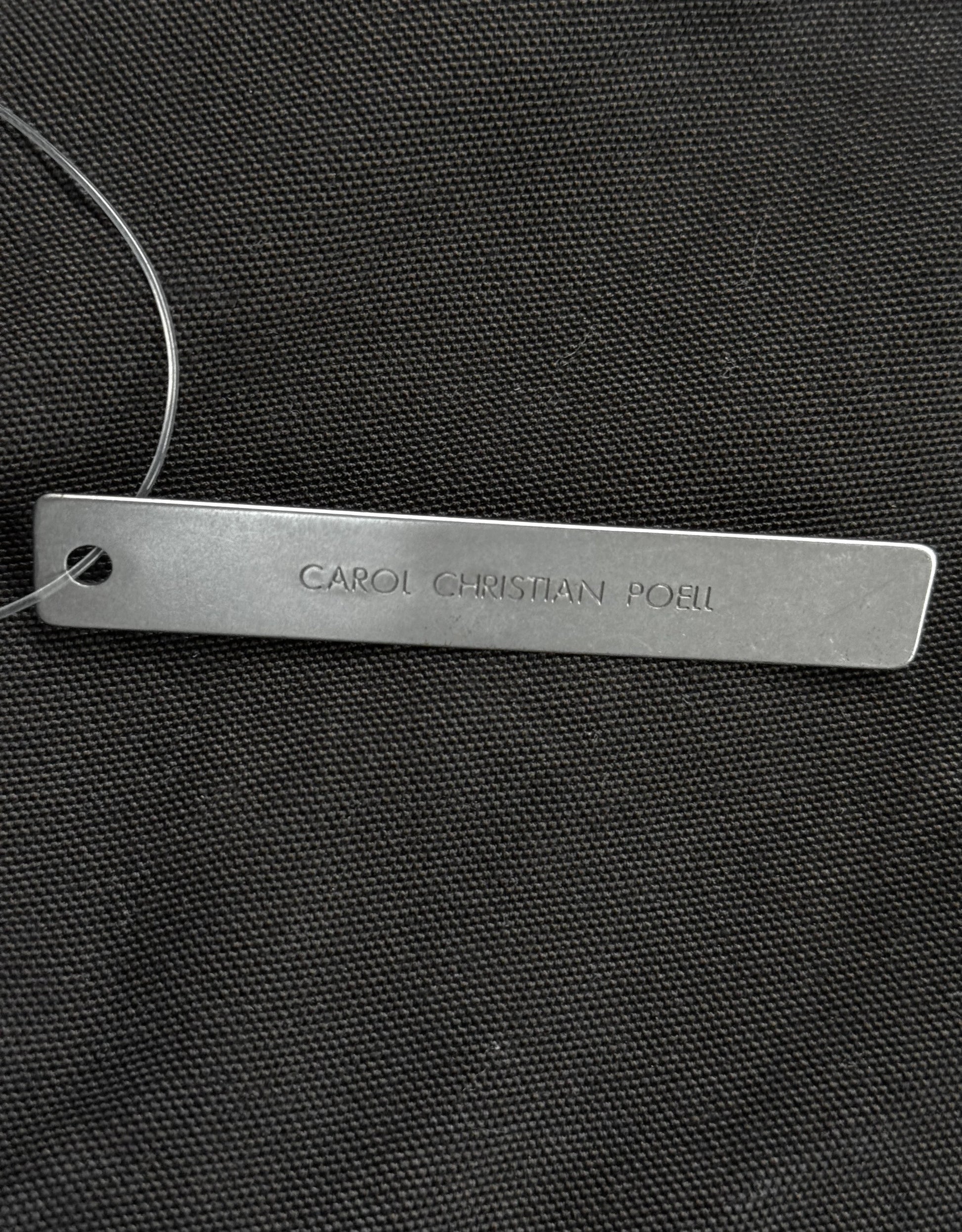Metal tag with 'CAROL CHRISTIAN POLO' engraved on a black textured background