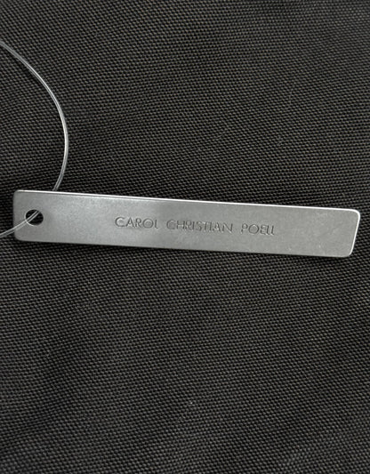 Metal tag with 'CAROL CHRISTIAN POLO' engraved on a black textured background