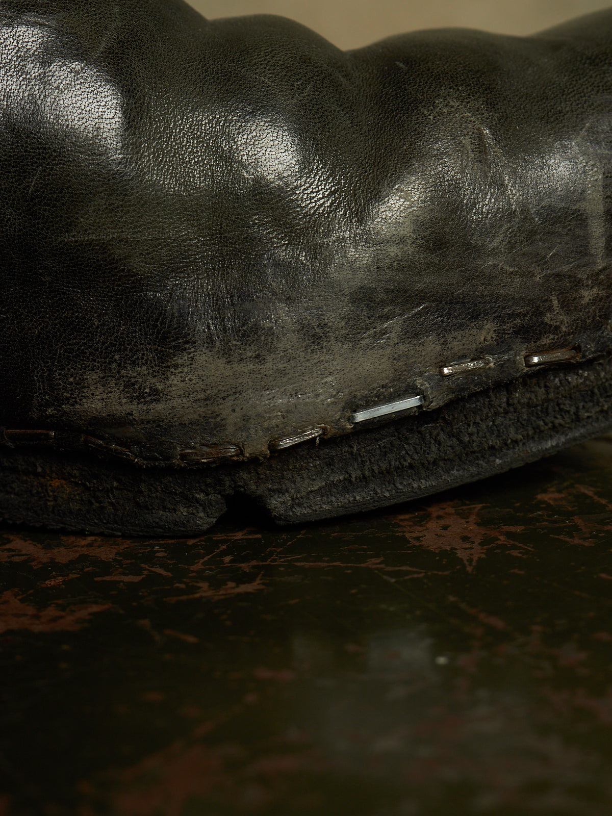 A close-up shot of a black leather boot or shoe sole with visible stitching and small metallic hardware, resting on a dark textured surface.