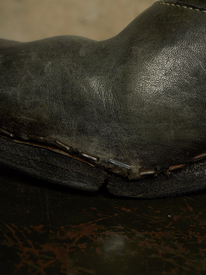 Close-up of a dark distressed leather boot showing the side profile, raw stitching, and sole edge.