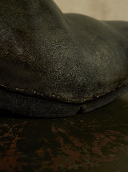A close-up shot of a dark, distressed leather boot or shoe sole showing the texture of the leather and the contrast stitching along the edge.