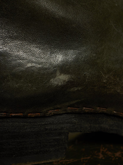 Close-up of a dark brown leather boot or shoe showing the textured grain, a stitched edge, and part of the dark sole.