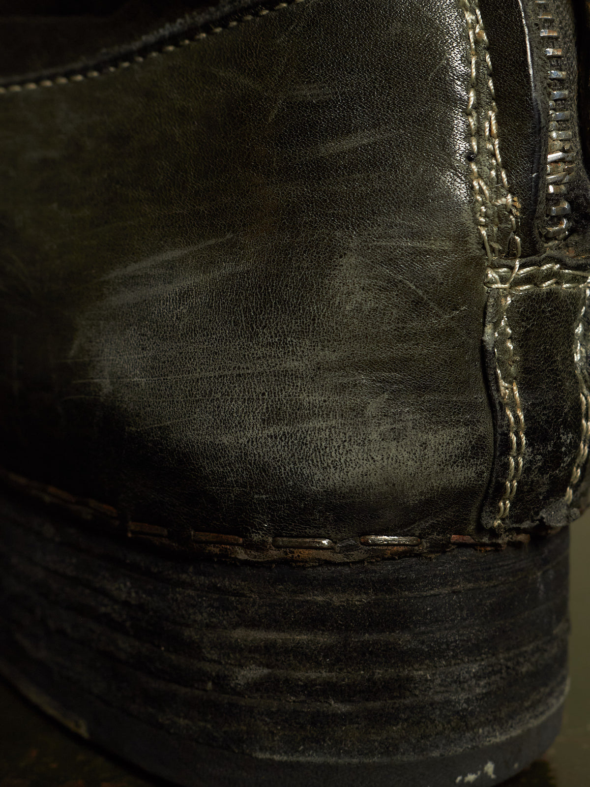 Close-up of a worn black leather boot showing the textured leather surface, contrast stitching, and a dark sole.