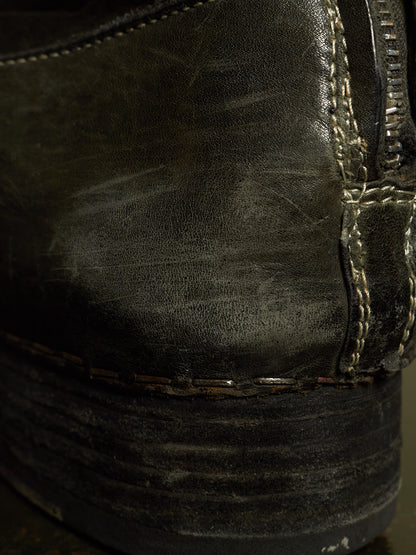 Close-up of a worn black leather boot showing the textured leather surface, contrast stitching, and a dark sole.