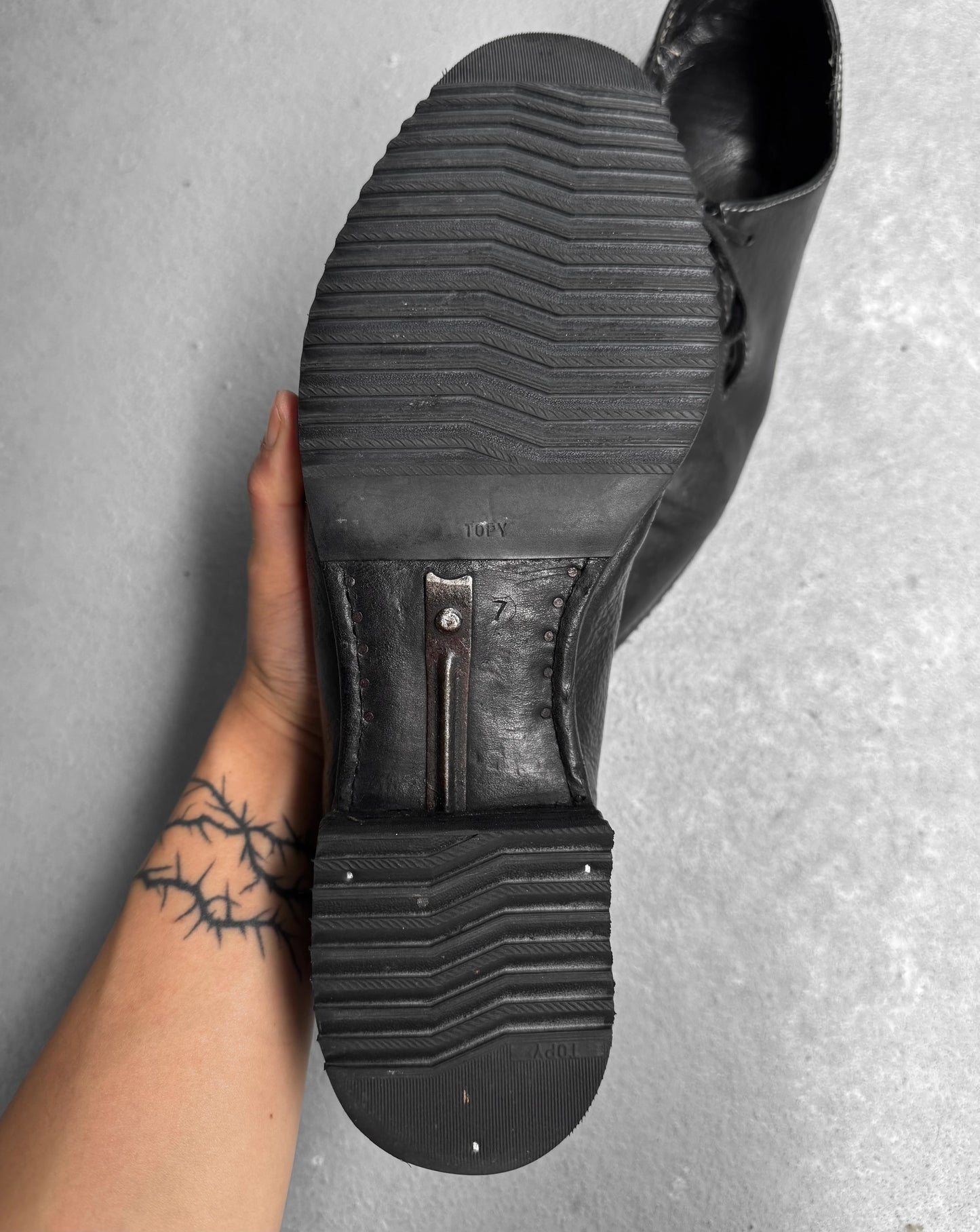 Black shoe being worn with a textured sole on a gray surface