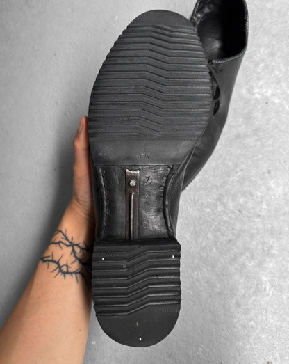Black shoe being worn with a textured sole on a gray surface