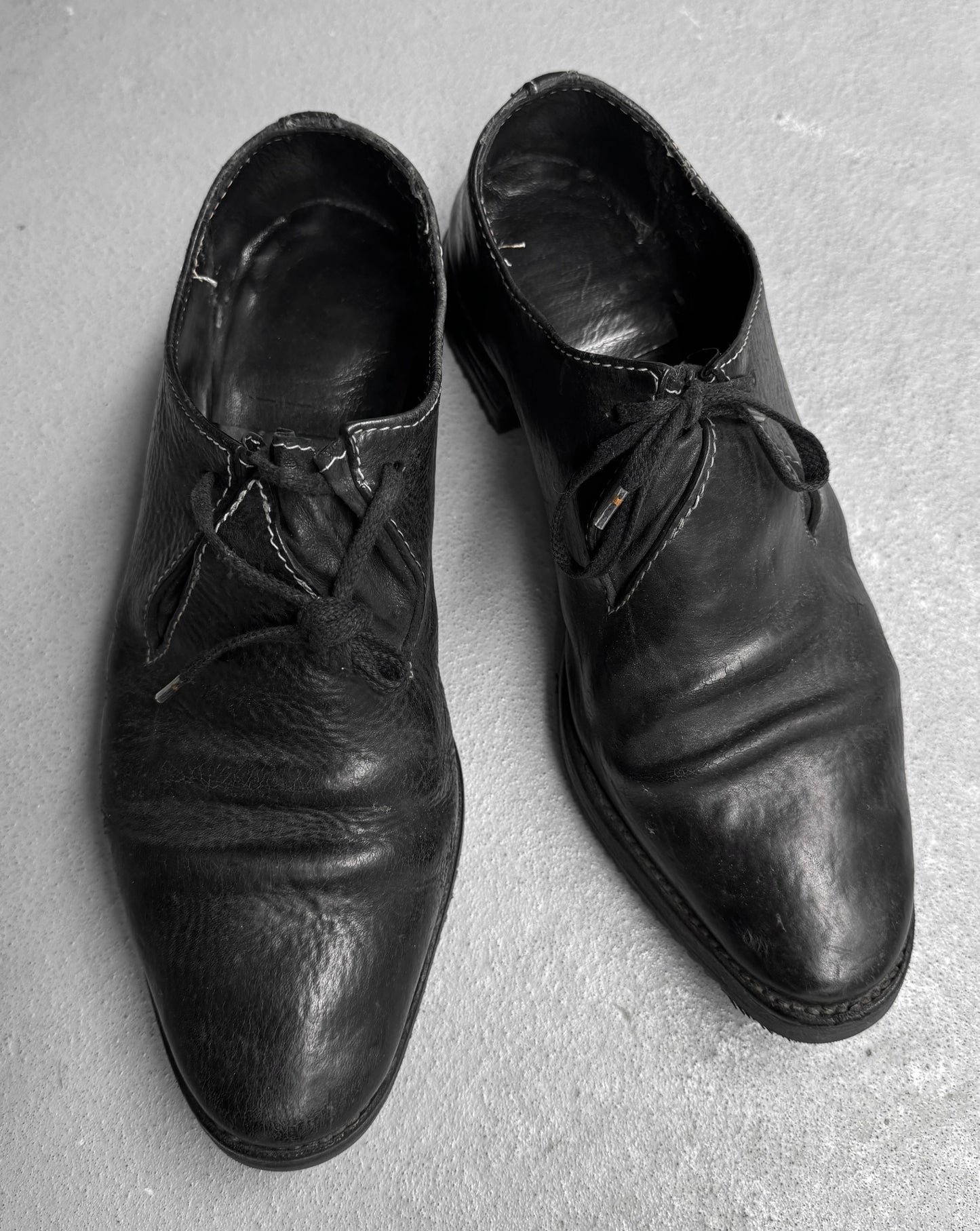 Pair of worn black leather shoes on a gray surface