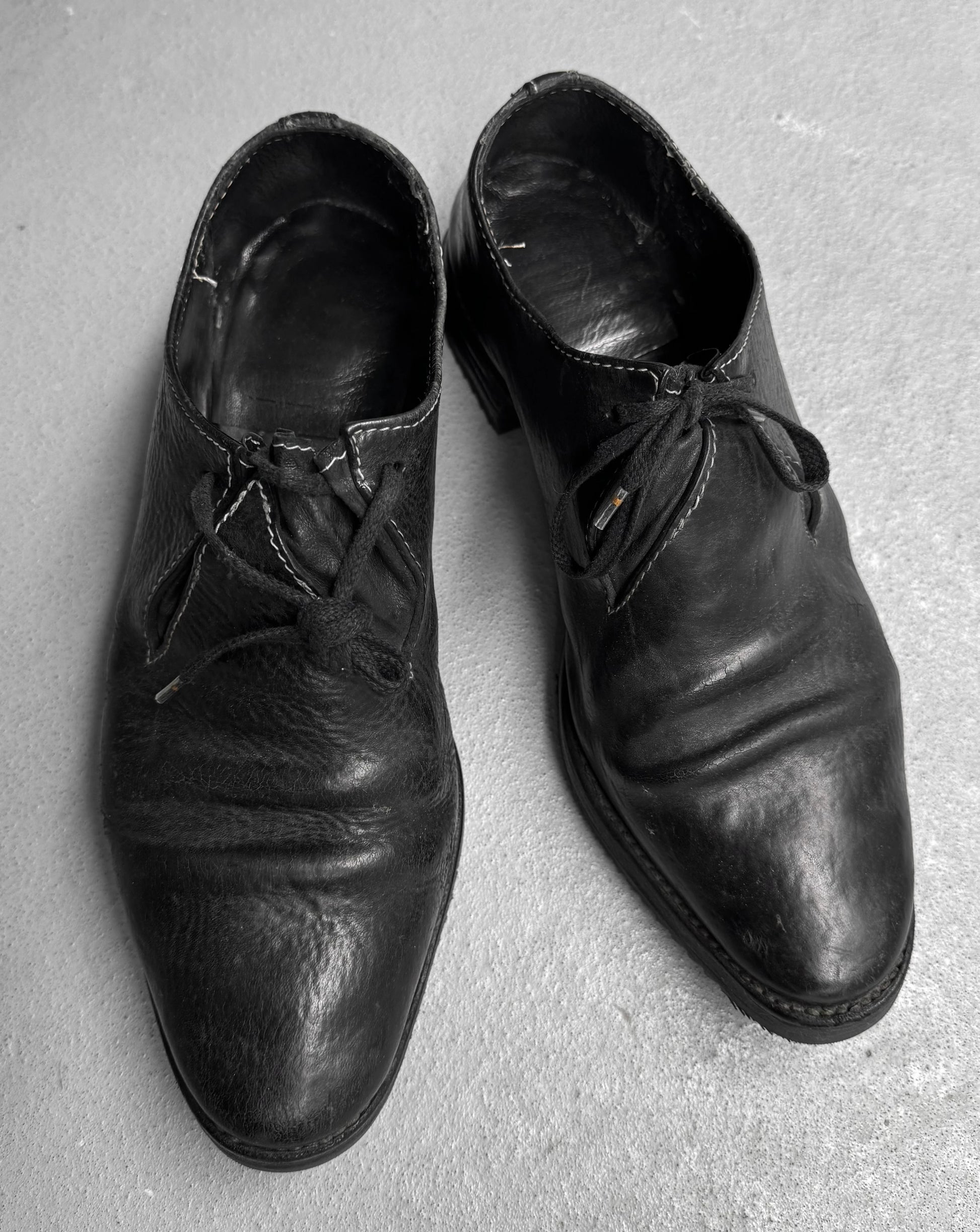 Pair of worn black leather shoes on a gray surface