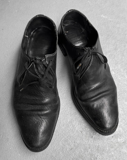 Pair of worn black leather shoes on a gray surface