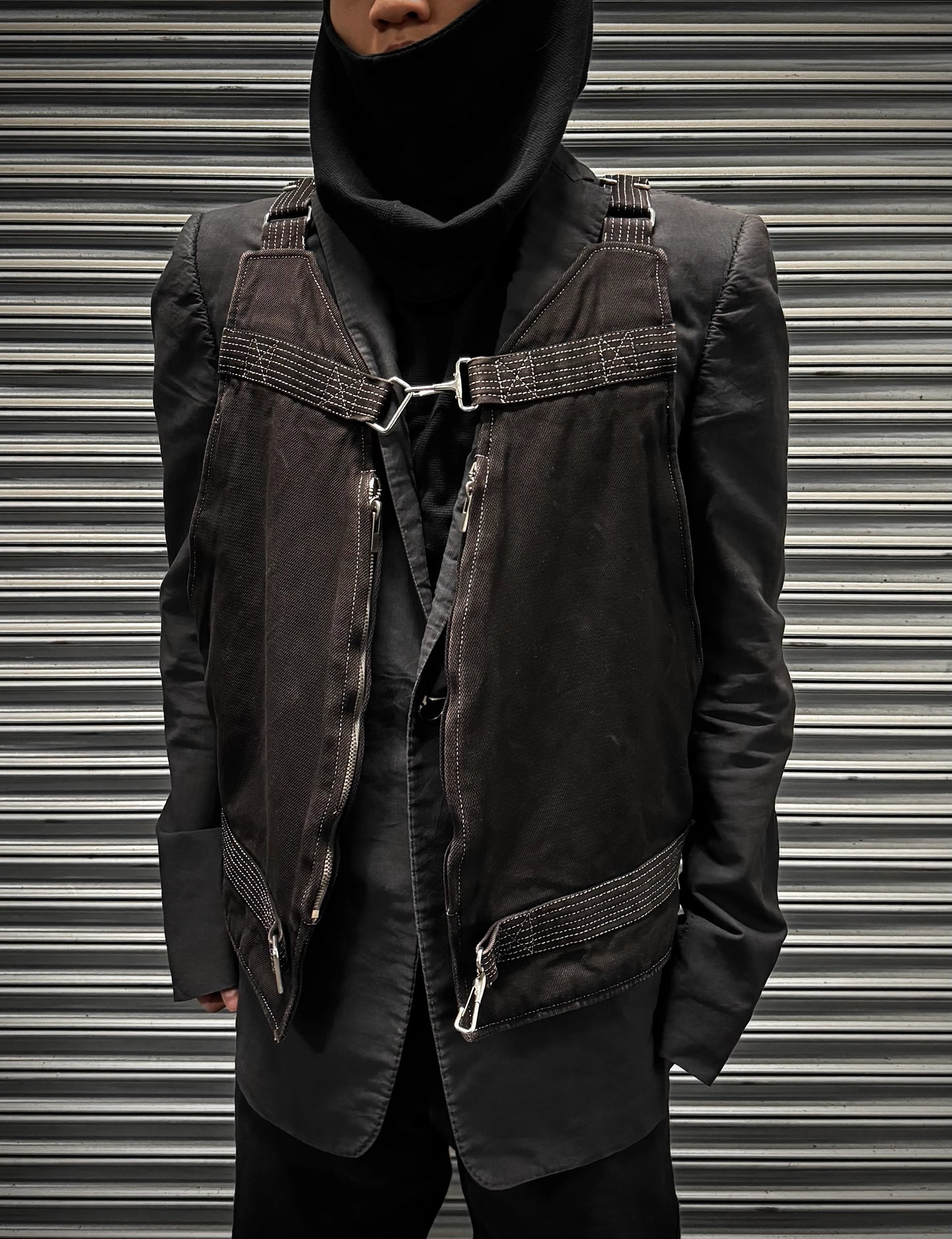 Person wearing a dark jacket with harness details against a metallic background