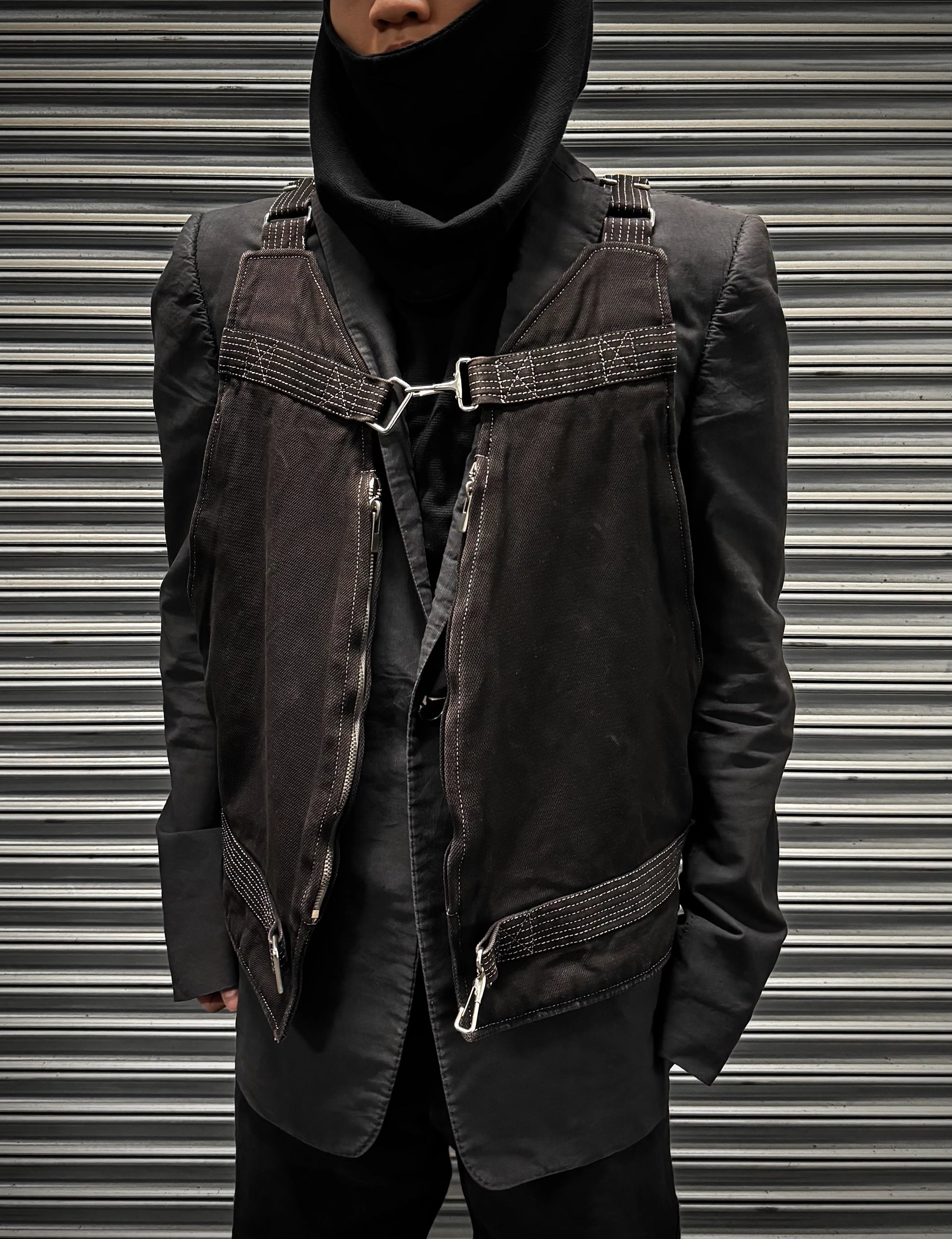 Person wearing a dark jacket with harness details against a metallic background