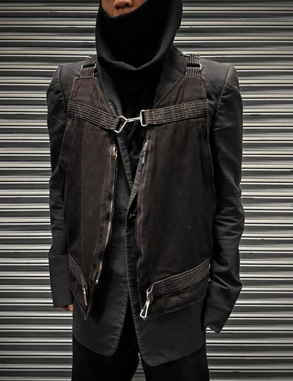 Person wearing a dark jacket with harness details against a metallic background