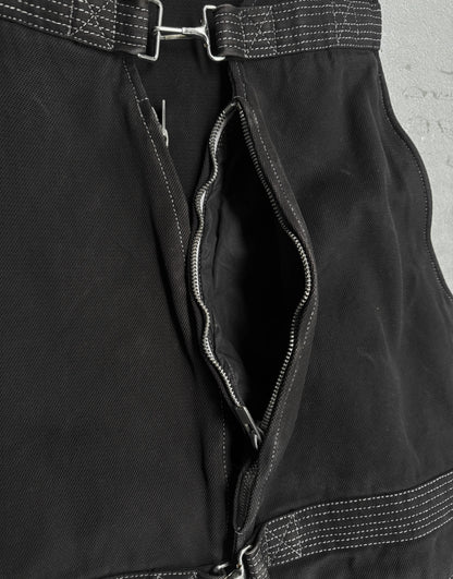 Close-up of a black jacket with a zipper and belt detail on a concrete surface.