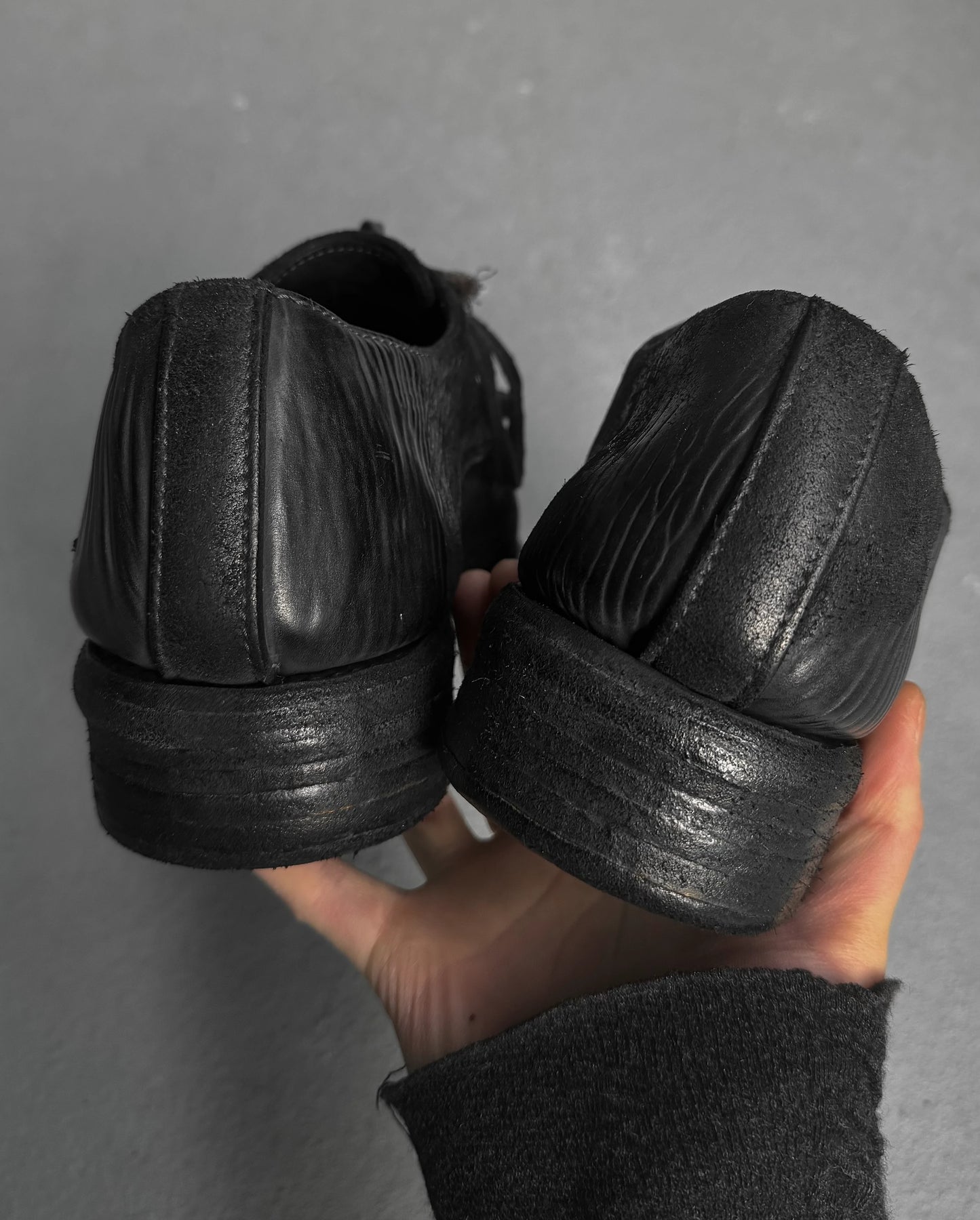 Black leather shoes held in a hand against a gray background