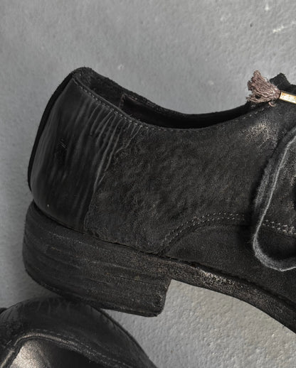 Black leather shoe with a small plant on a gray background