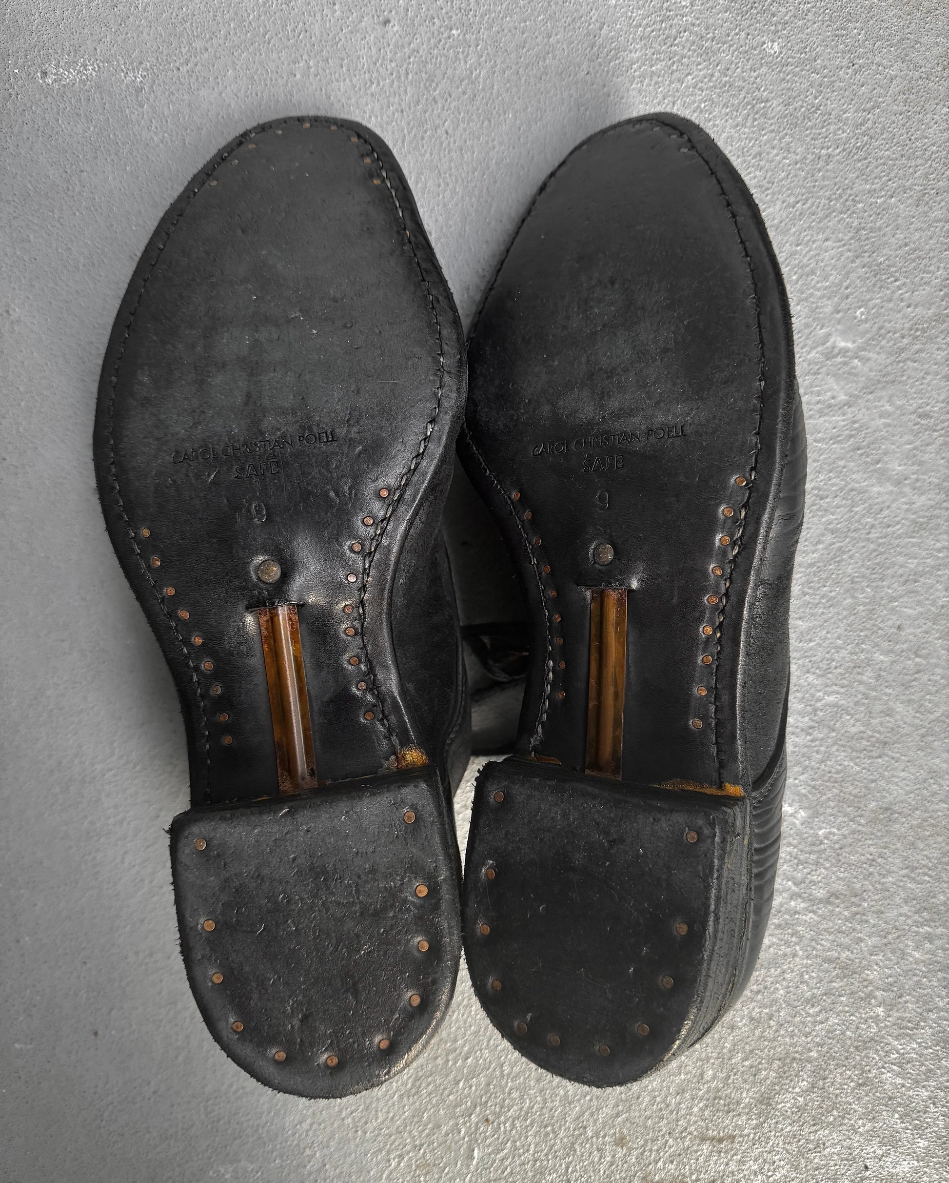 Pair of black leather shoes with brown soles on a gray surface