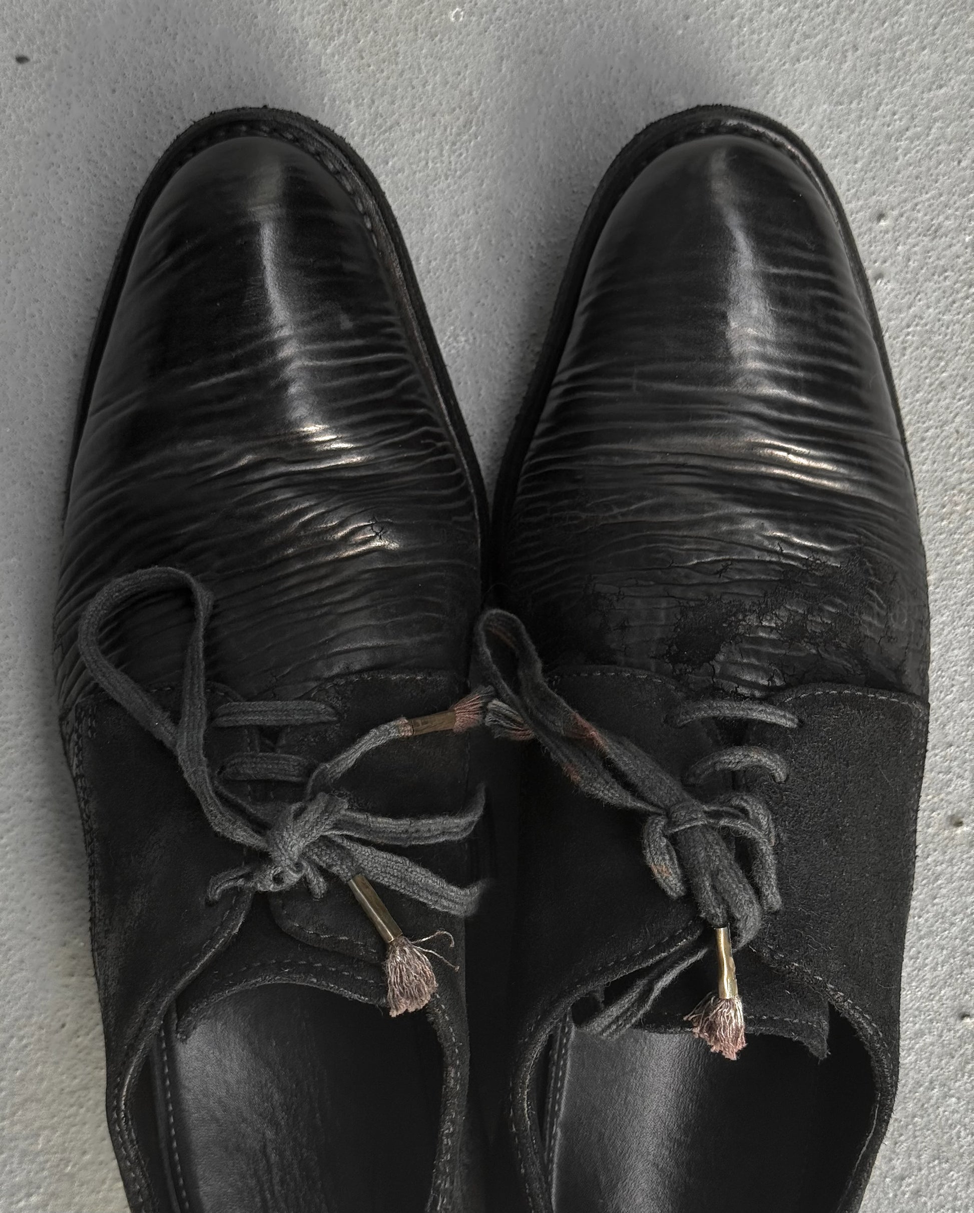 Pair of black leather shoes with worn laces on a gray surface