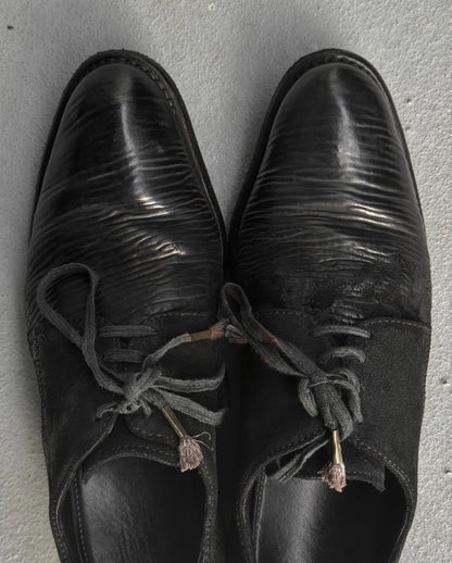 Pair of black leather shoes with worn laces on a gray surface