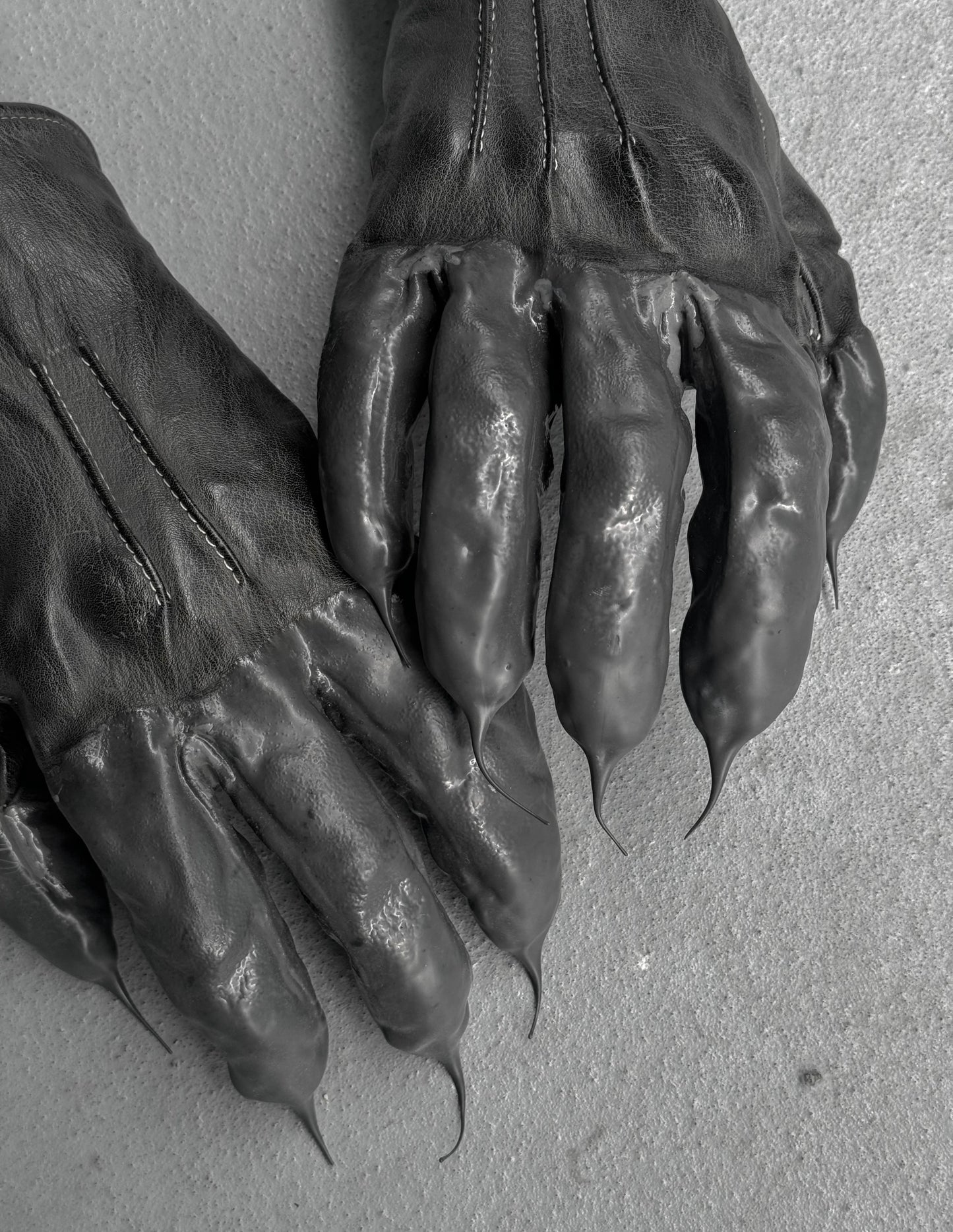 Pair of dark leather gloves with clawed tips on a light gray background