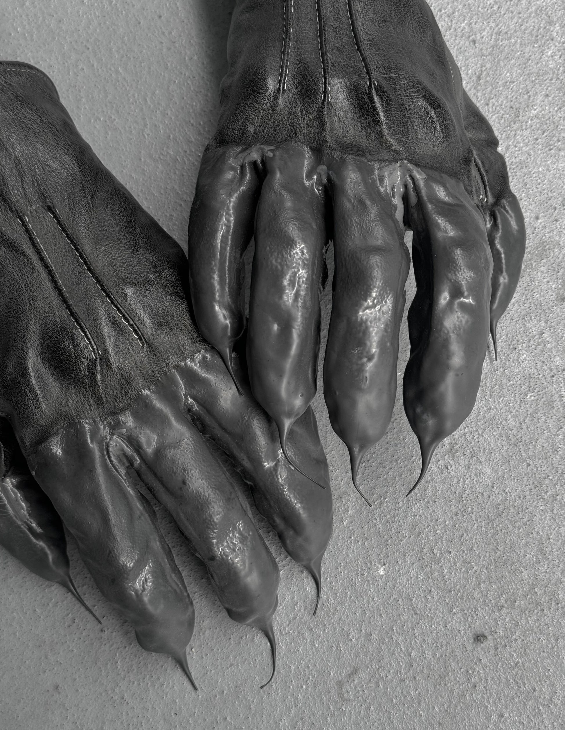 Pair of dark leather gloves with clawed tips on a light gray background