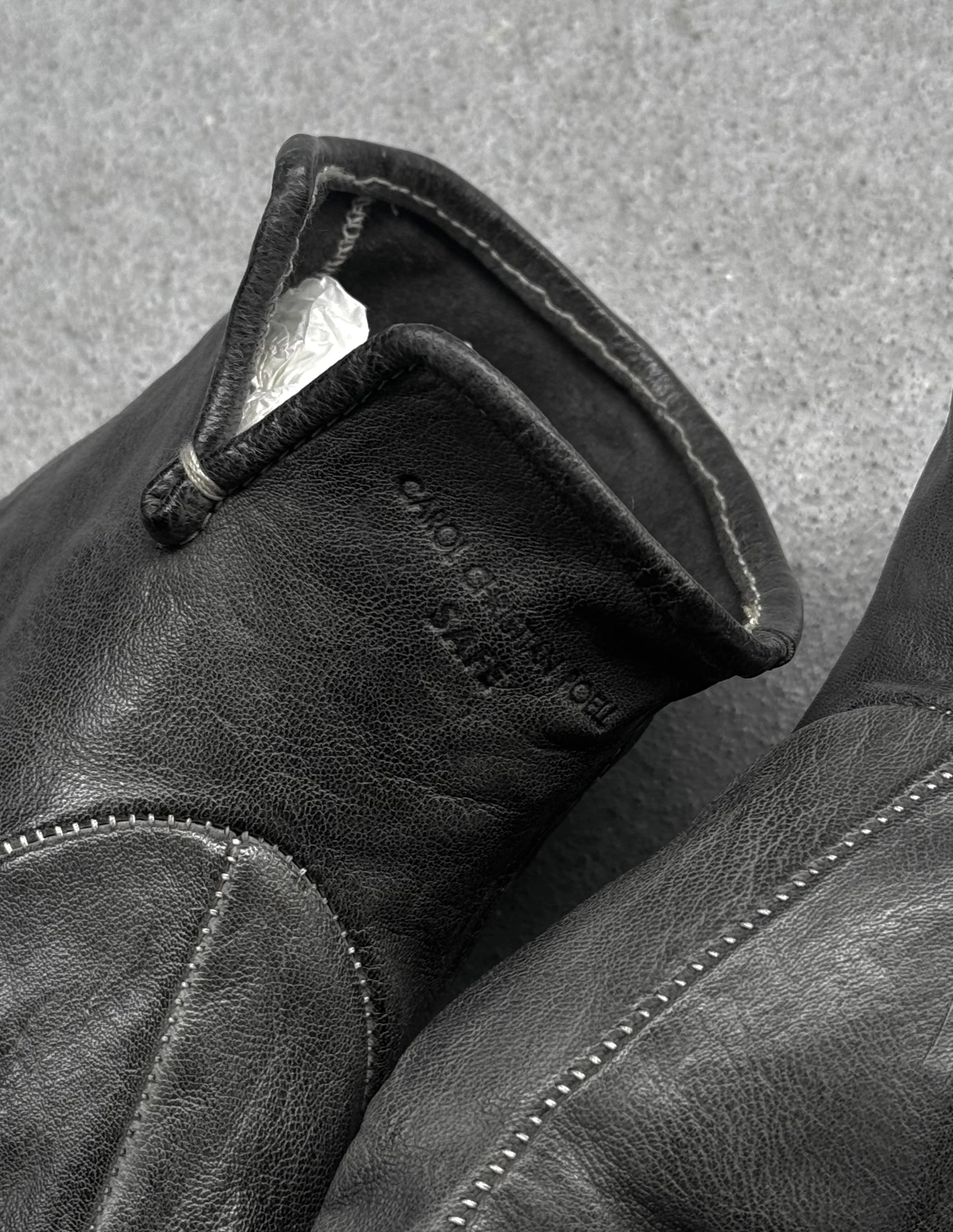 Close-up of a black leather glove with visible stitching on a textured gray background