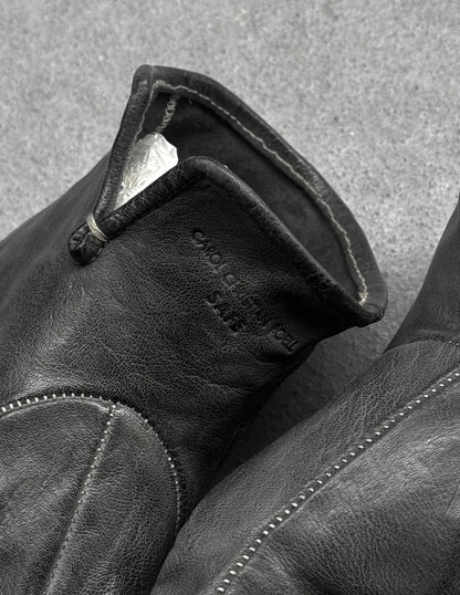 Close-up of a black leather glove with visible stitching on a textured gray background