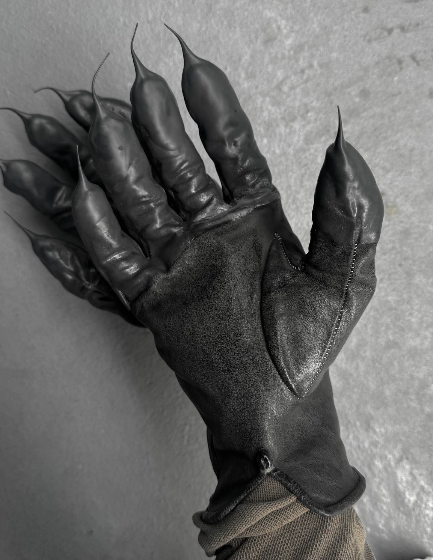 Black leather glove with clawed fingertips on a gray background