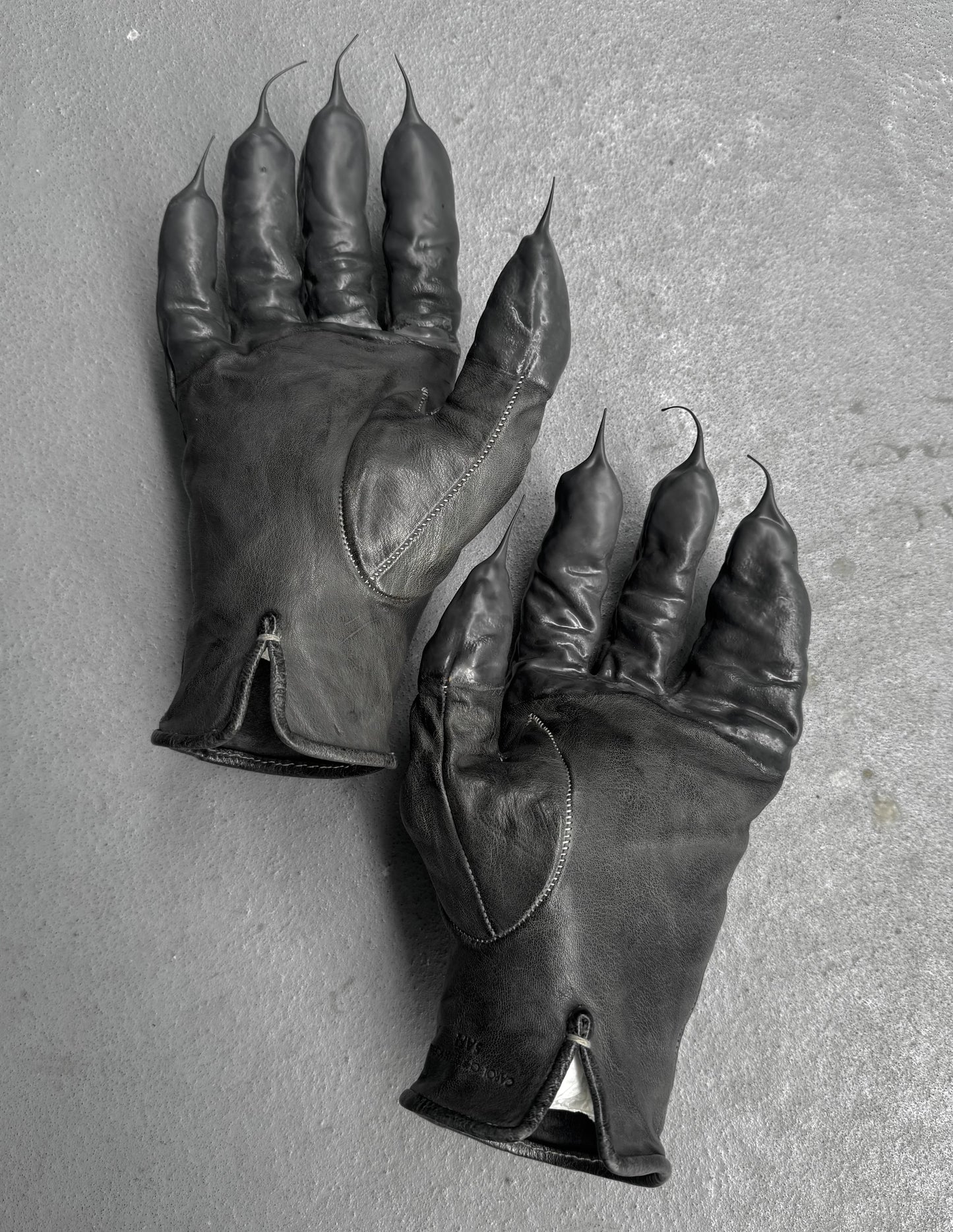 Pair of black leather gloves with clawed fingertips on a gray background