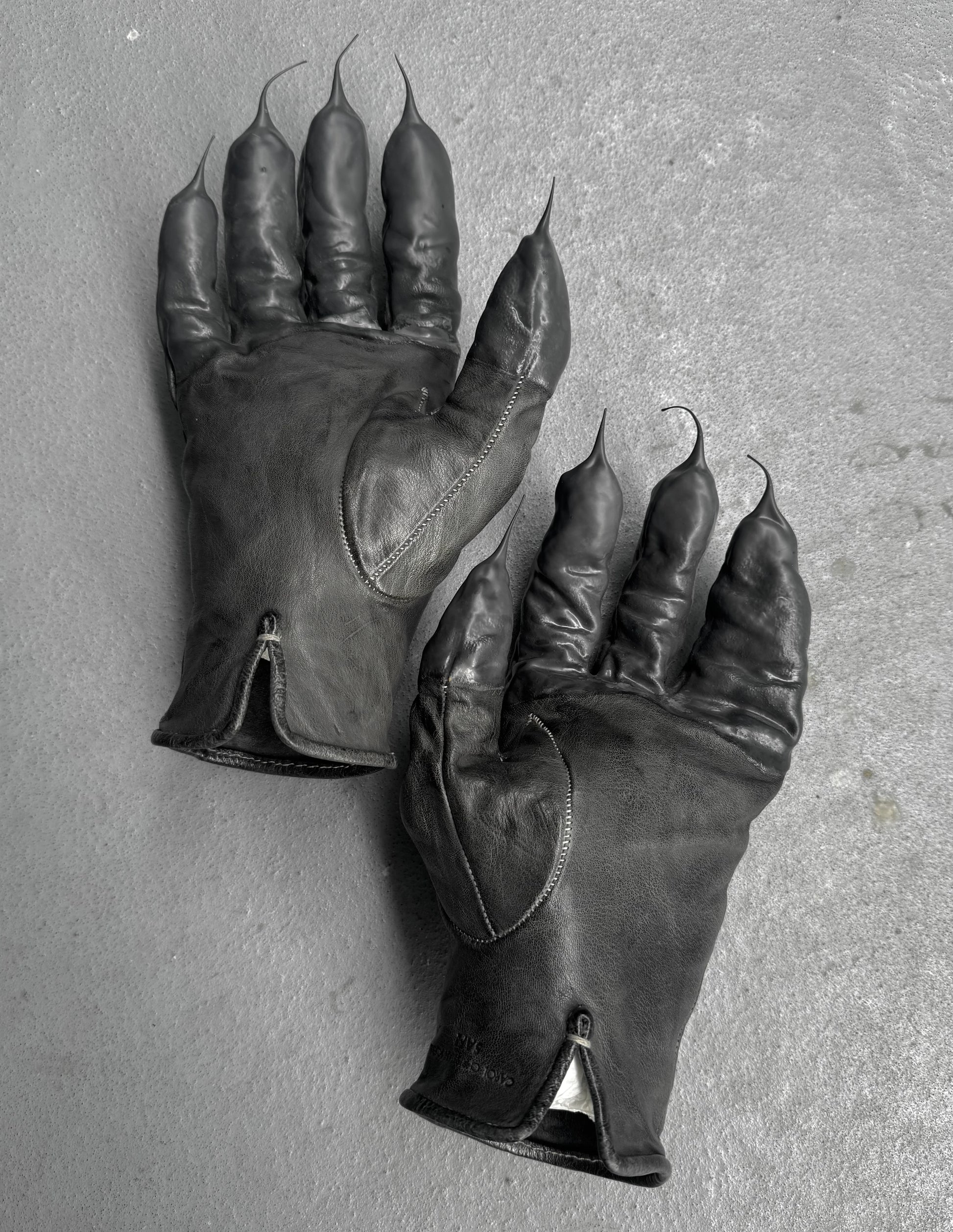 Pair of black leather gloves with clawed fingertips on a gray background