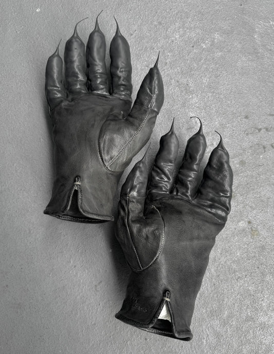 Pair of black leather gloves with clawed fingertips on a gray background