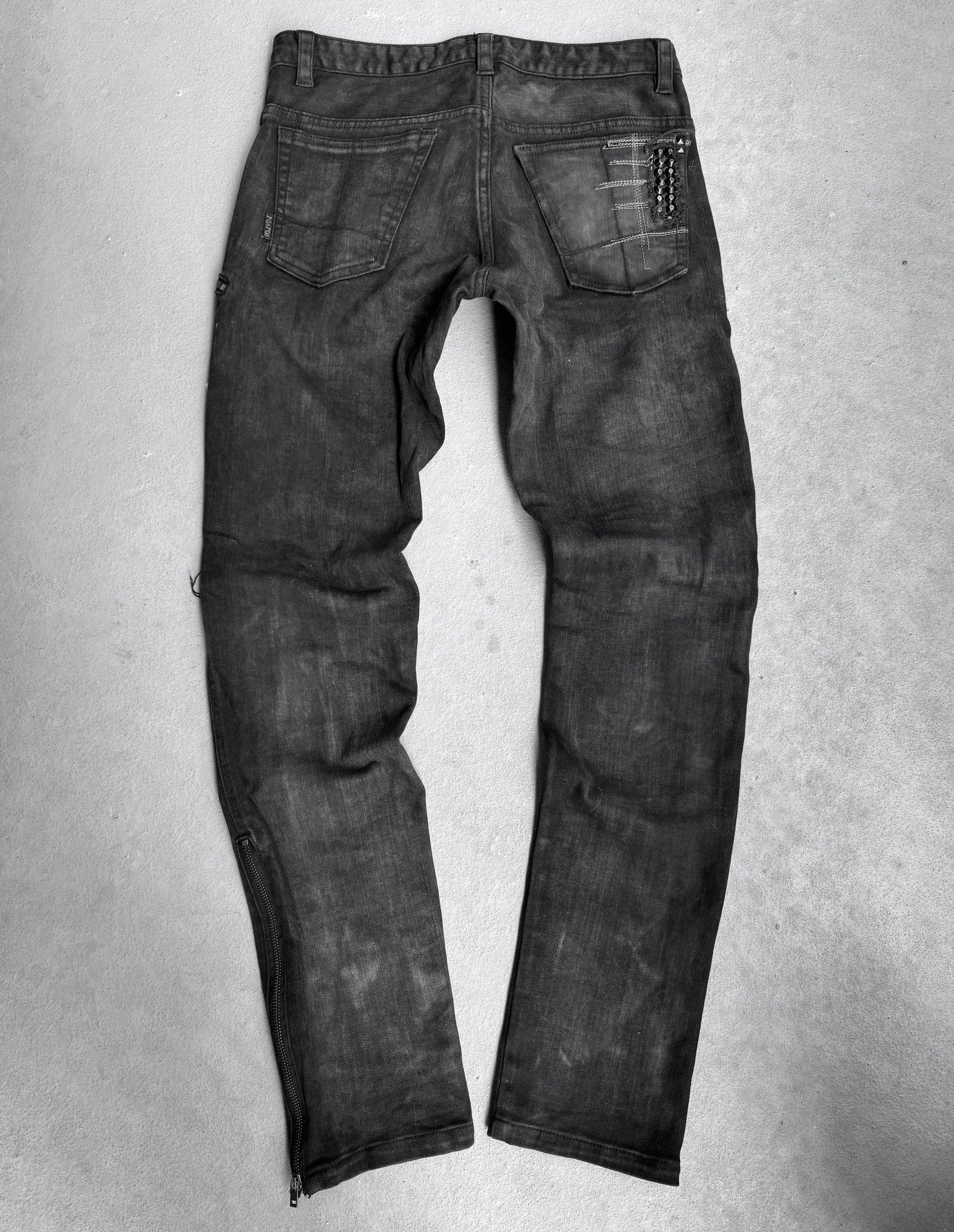 A pair of KMRii Early 00s Goatskin Patches Studded Crush Flare-zip Denim jeans, size 2 (fits US 29-30 waist), black with slight fading, shown from the back with two back pockets and a chain on the right pocket, lies flat on a light grey surface.