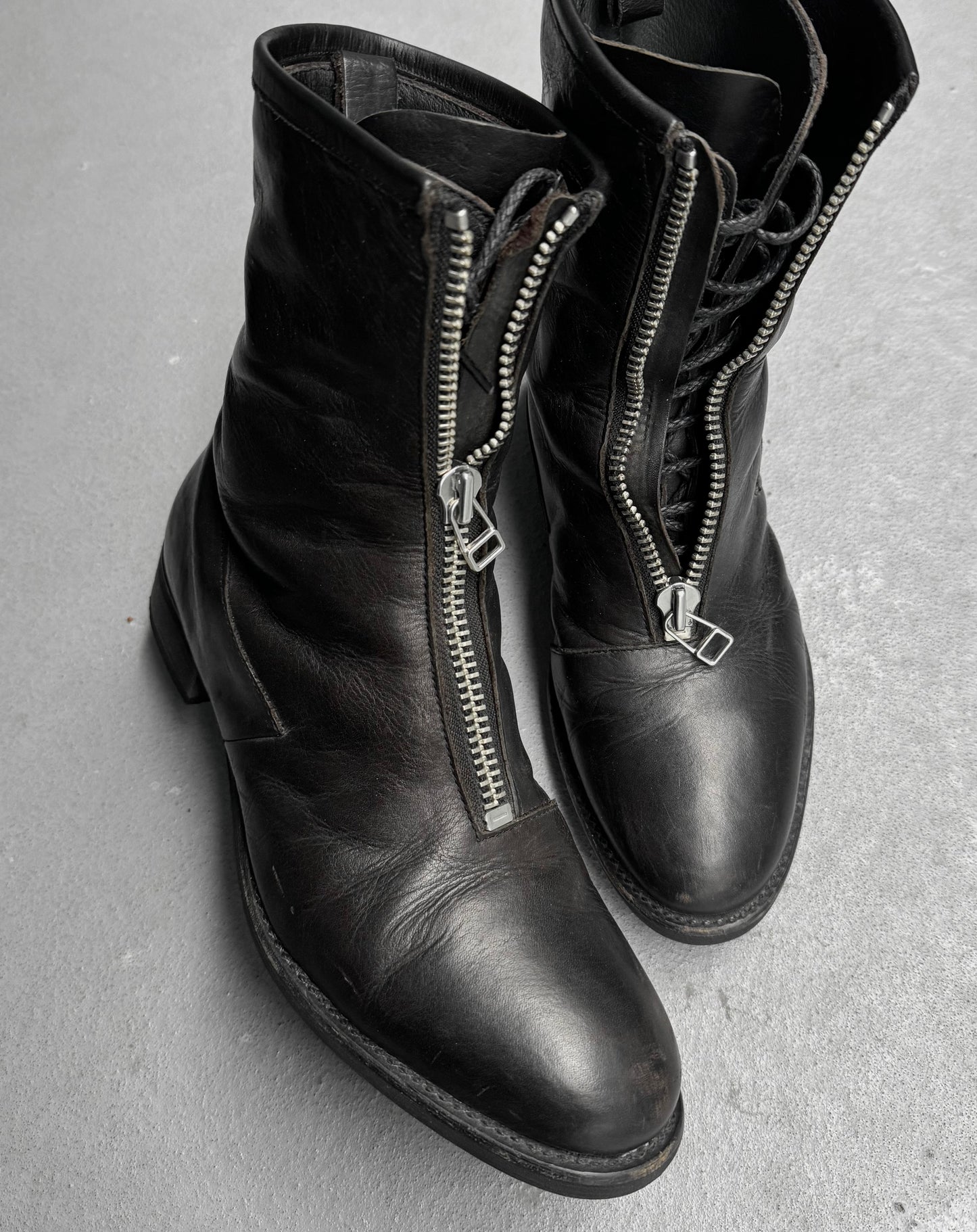 Black leather boots with zippers on a gray surface