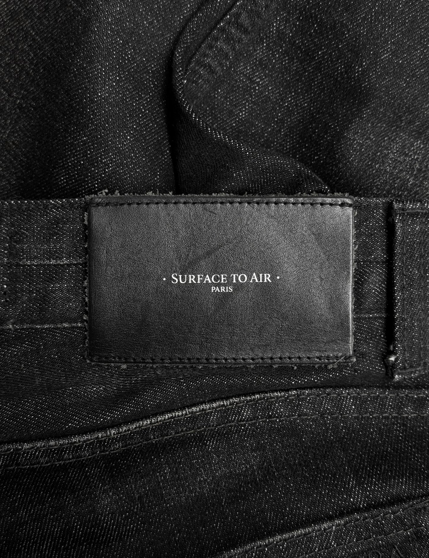 Close-up of a black leather label stitched onto the Surface To Air SS14 Faded Black Bootcut Skinny Denim, featuring the brands name and reflecting its contemporary urban menswear style.