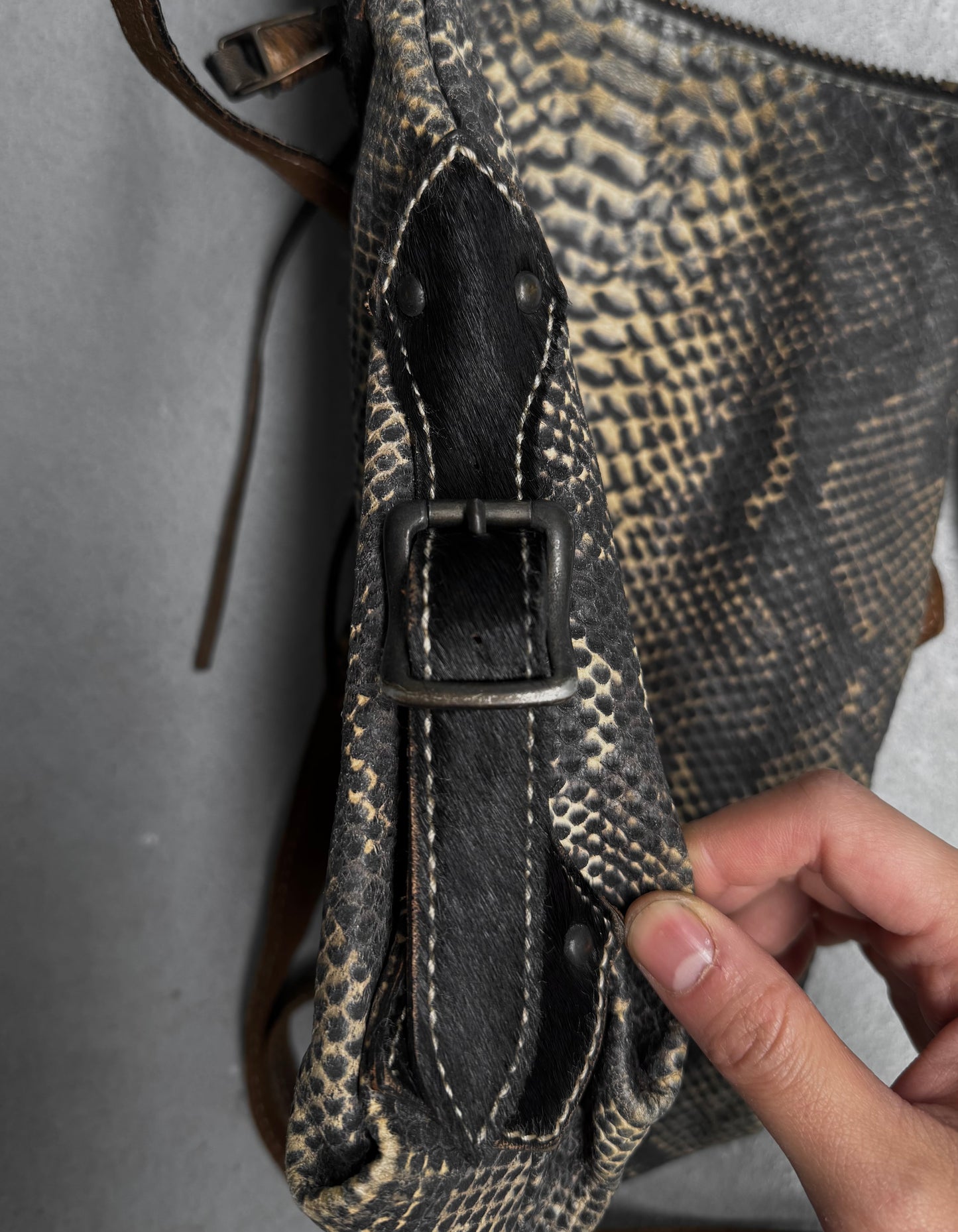 A close-up of a hand holding the side strap of a Kyoji Maruyama Early 00s Yellow Crocodile Embossed Leather Side Bag, featuring textured leather, visible stitching, and a metal buckle.
